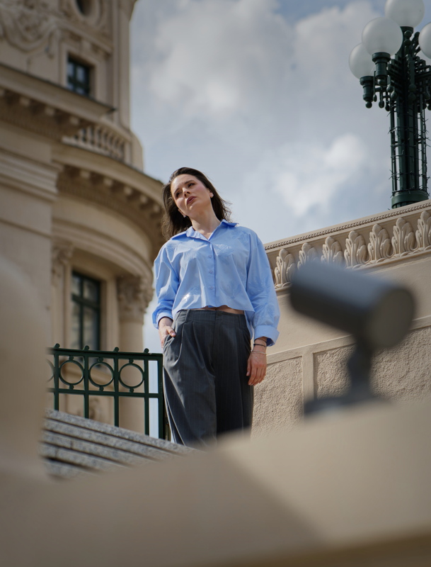 Woman posing in a blue button-down shirt and grey trousers on a stone staircase